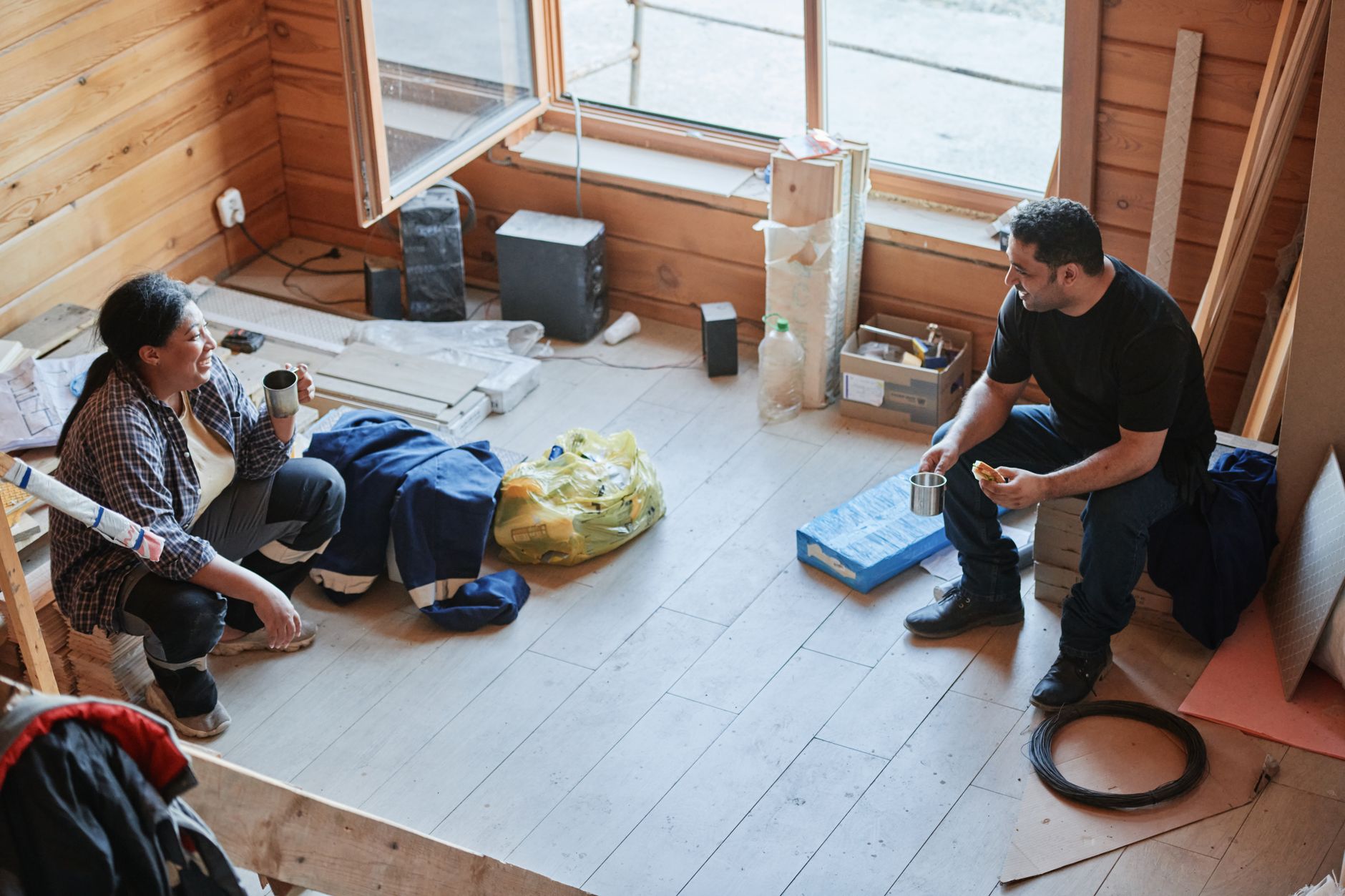 Two construction workers taking a break and chatting inside a wooden room during a renovation project.